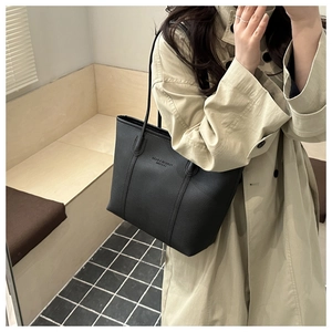 Close-up of black lychee texture tote bag with minimalist lettering on model's shoulder