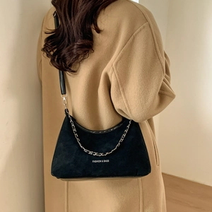 Black crescent underarm bag with silver chain detail shown on shoulder with coat
