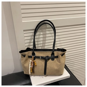 Close-up of beige faux suede tote bag with black leather straps and retro beaded charm