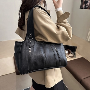 Large black leather tote bag with side pockets and wide strap on model in urban room