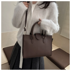 Detail of dark brown tote bag in lychee texture leather worn by a model in a minimalist setting