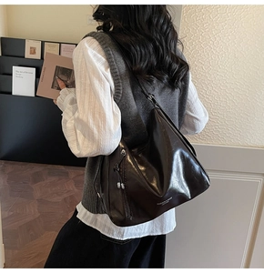 Detail of dark brown glossy leather tote bag with side zipper and circular pendant
