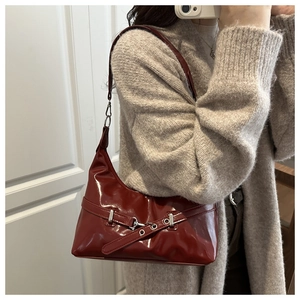 Detail of dark red glossy underarm bag featuring silver metal buckle and sleek leather straps