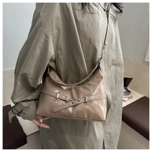 Detail of glossy beige shoulder bag featuring decorative metallic buckle and sleek patent finish