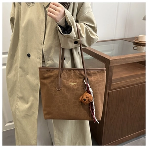 Detail of leopard print tote bag with plush dog charm and scarf on a beige trench coat