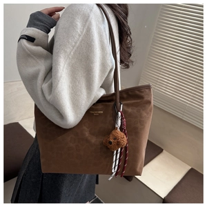 Detail of a large brown suede tote bag with a plush bear charm and leather straps