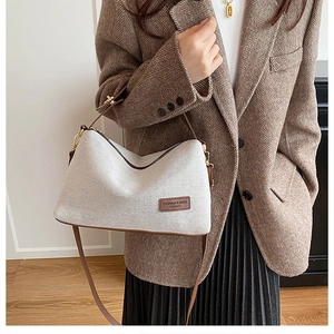 Detail of canvas shoulder bag with brown leather trim and fashion label on front