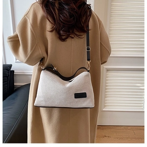 Detail of beige textured shoulder bag with fashion label and black leather strap