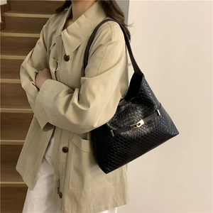 Borsa hobo nera intrecciata con fibbia dorata indossata con un trench beige elegante