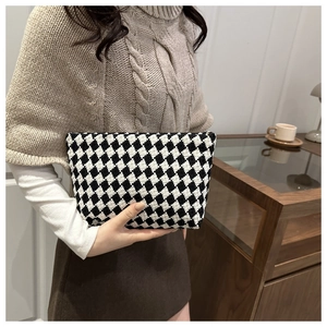 Detail shot of black and white checkered tweed clutch bag held by a model