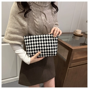 Black and white checkered tweed clutch bag held by model wearing a knit shawl