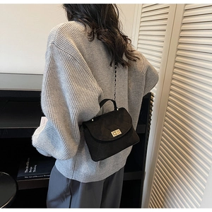 Side view of a quilted black crossbody bag with gold lock on a model in a minimal room