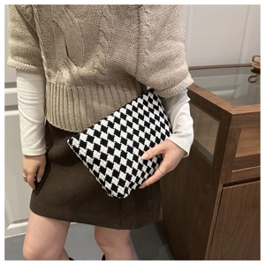 Detail of a chic black and white houndstooth wool clutch bag held by a model in winter wear