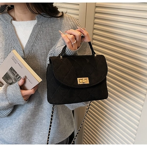 Detail of black quilted handbag with gold twist lock and woven chain strap on model