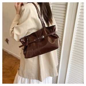 Detail of glossy brown oversized tote bag with silver buckle strap and shoulder carry