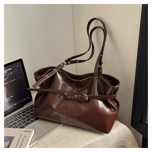 Close-up of deep brown glossy leather tote bag with adjustable buckle strap and belt decor
