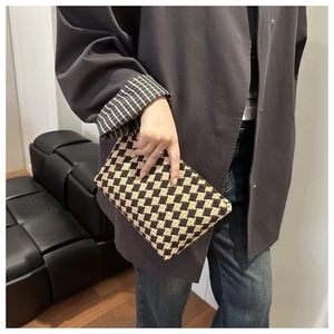 Close-up of a woven clutch bag with brown and beige checkered patterns held by a model