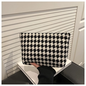 Close-up of black and white houndstooth textured clutch bag held by a person