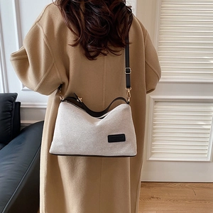 Beige woven crossbody bag with black leather straps shown on a model in a warm wool coat