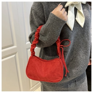Détail du sac bandoulière en daim rouge avec anse froncée et nœud décoratif élégant