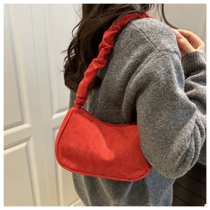Détail de la bandoulière froncée du sac rouge en suédine sur un pull gris foncé