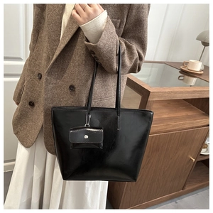 Detail of a black glossy large tote bag with a small hanging purse on model