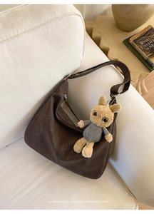 Detail of dark brown matte leather tote bag on sofa with cute plush bunny pendant accessory