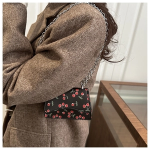 Detail of mini saddle bag featuring cherry print on black leather with silver chain strap