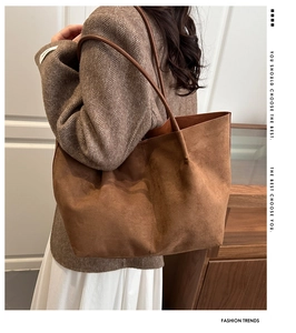 Detailed view of the large brown suede tote bag worn on a model's shoulder in soft lighting