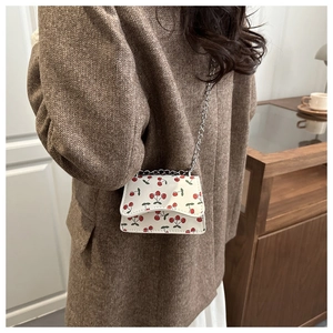 Close-up of white mini crossbody bag with red cherry print and silver chain strap details
