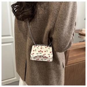 Mini crossbody bag with red cherry print and silver chain strap shown on model