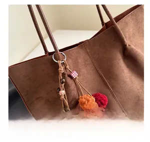 Detail of vintage brown suede tote bag featuring a colorful beaded pompom charm accessory