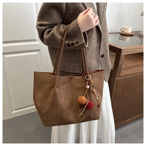 Detail of a large dark brown suede tote bag with a retro pompom charm and leather straps