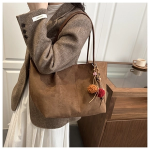 Detail of a large brown suede tote bag featuring a vintage bohemian tassel and pompom charm