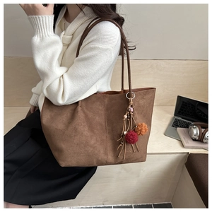 Detailed close-up of brown suede tote bag with decorative colorful pompom and tassel