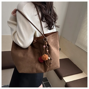 Detail of dark brown suede tote bag featuring colorful fur ball and fringe bag charm