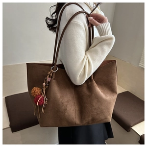 Close-up of brown suede tote bag featuring a decorative colorful fur ball charm