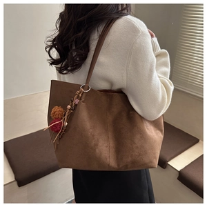 Detail of brown suede tote bag featuring ethnic tassel charm with colorful pom-poms