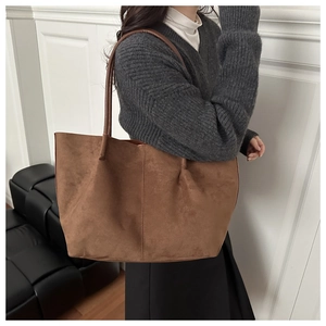 Detailed close-up of a large brown suede tote bag featuring slim leather shoulder straps