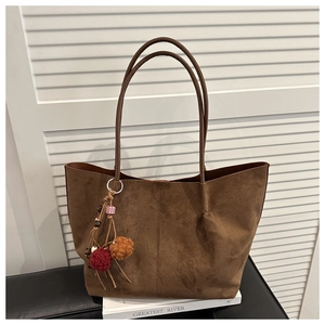 Detail of a brown faux suede tote bag with a colorful plush pom-pom and wooden bead charm
