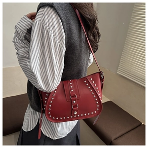 Detail of red leather shoulder bag featuring silver rivets and adjustable strap design