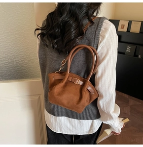 Close-up of brown suede tote bag featuring decorative belt buckle and vintage leather strap