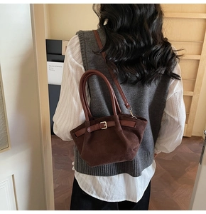 Detail of dark brown suede handbag with leather strap and metal buckle on a model