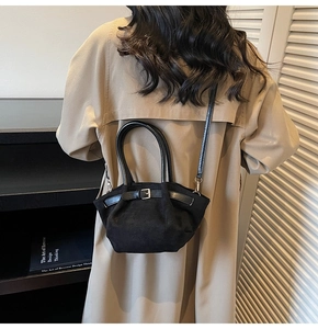 Detail of a black suede dumpling bag with a silver buckle worn with a beige trench coat