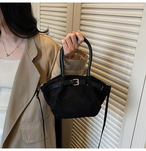 Detail of a chic black suede dumpling bag with silver buckle worn with a trench coat