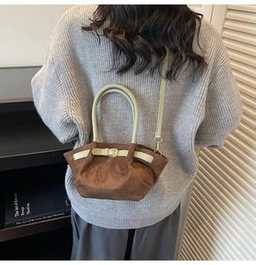 Detail of suede handbag in dark brown with sage green leather trim and golden buckles