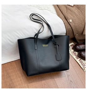 Detail shot of black leather tote bag with gold lettering and shoulder straps on soft bedding