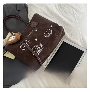 Detail van donkerbruine suède tote bag met kattenborduursel en pluche leeuwenhanger