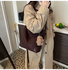 Détail du sac hobo en daim marron foncé avec coins en cuir renforcés et breloque petit ourson