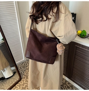 Détail du sac à bandoulière en daim marron foncé avec coins renforcés et breloque ourson